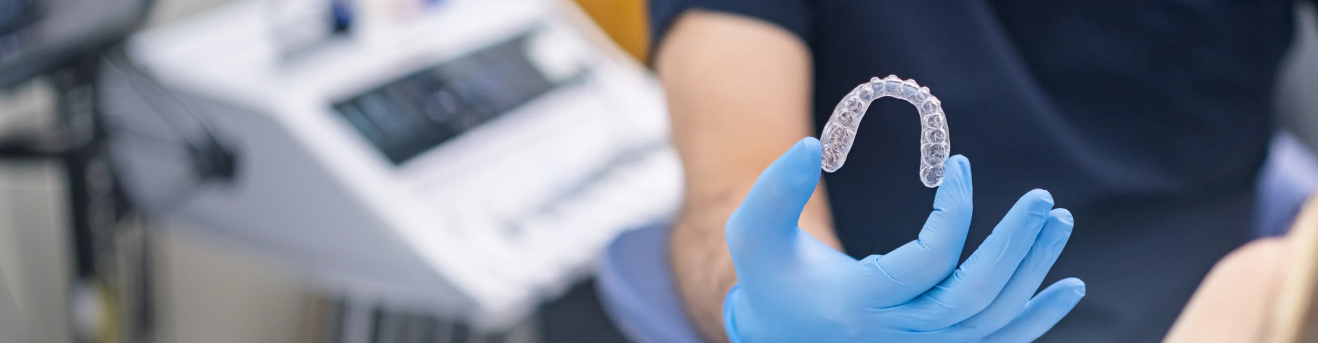 Gloved hand holding clear aligner.